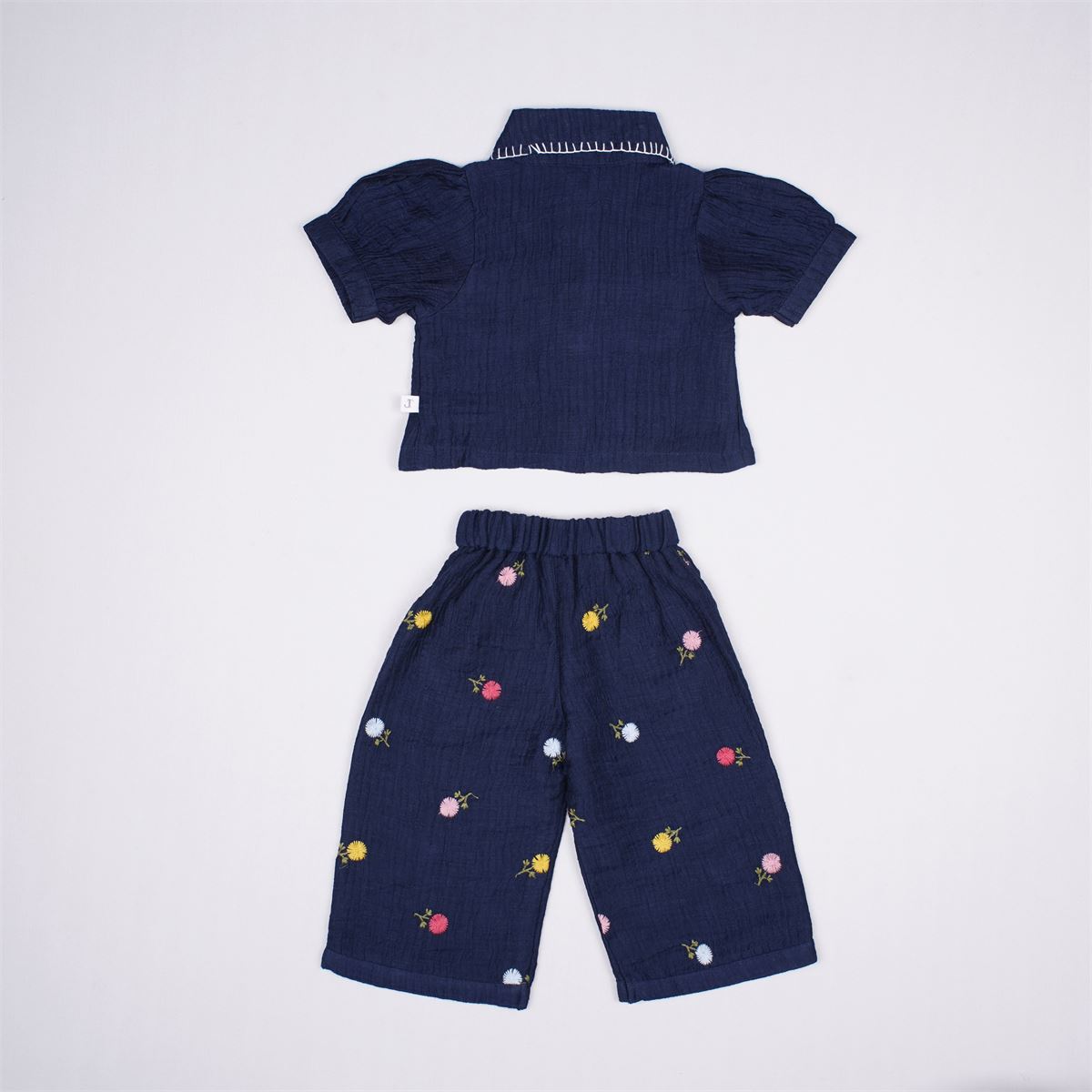 Justtots A chic two-piece navy blue textured cotton set featuring a stitch-detailed button-down shirt and matching floral embroidered trousers with tassel pockets.